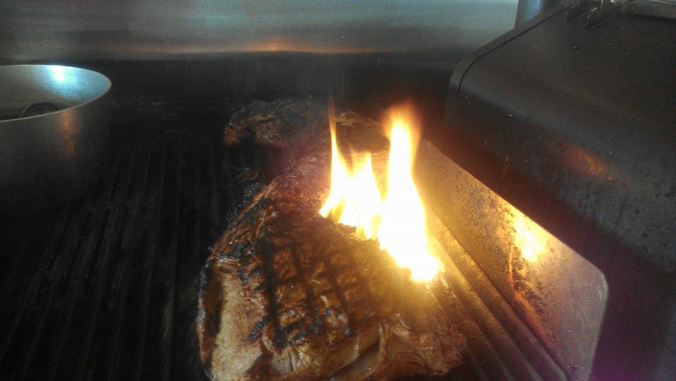 A slab of beef being grilled over open flame.